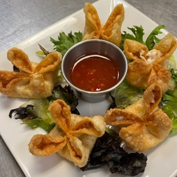 Golden-fried crab rangoons with sweet chili dipping sauce and lettuce on a white plate.
