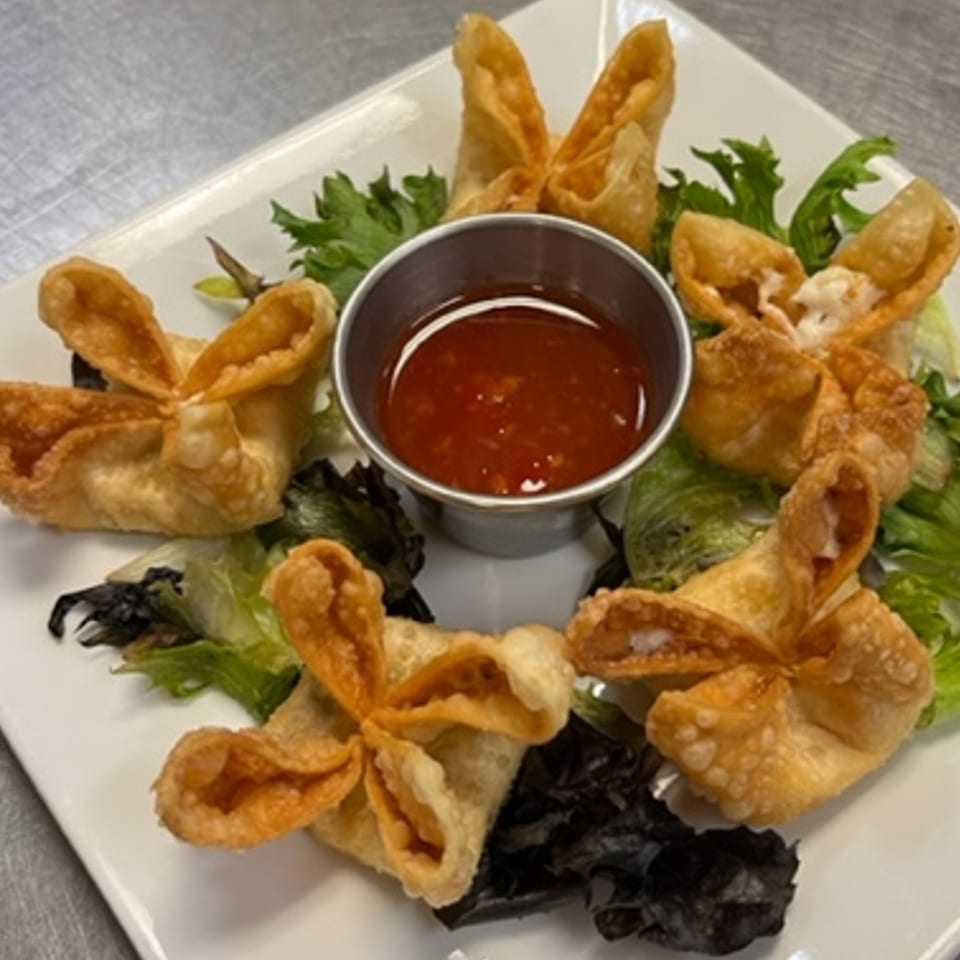 Golden-fried crab rangoons with sweet chili dipping sauce and lettuce on a white plate.