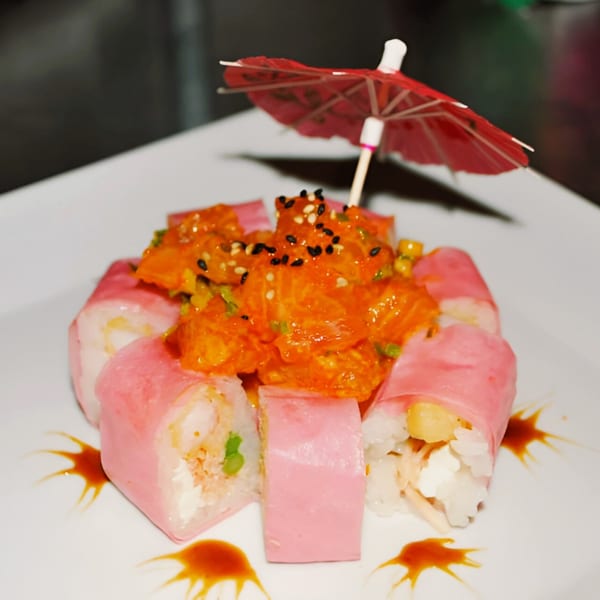 Pink sushi rolls with a spicy orange topping and a small red umbrella on a white plate.