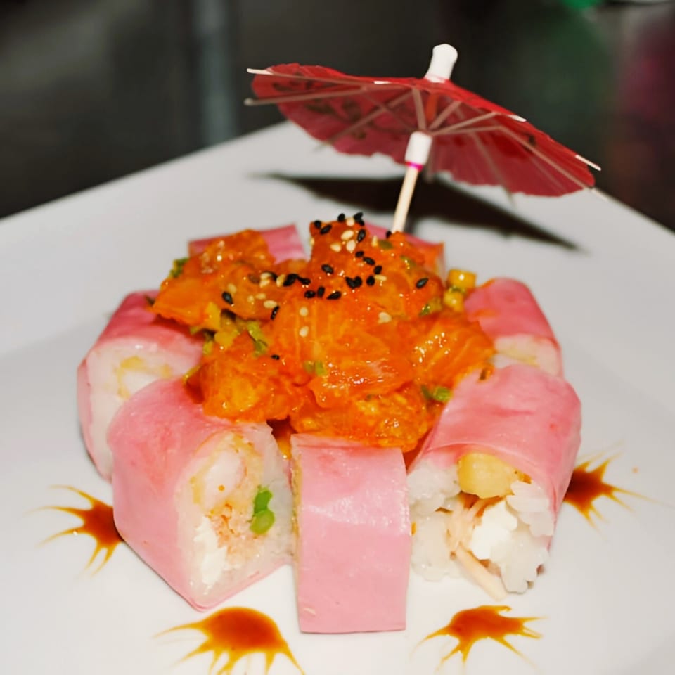 Pink sushi rolls with a spicy orange topping and a small red umbrella on a white plate.