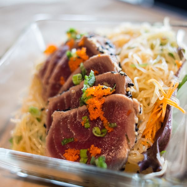 Seared tuna slices with roe, scallions, and sesame seeds, served over noodles and shredded carrots.