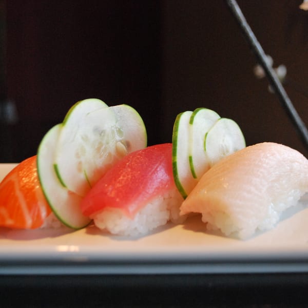 Three pieces of sushi with salmon, tuna, and white fish, garnished with cucumber slices.
