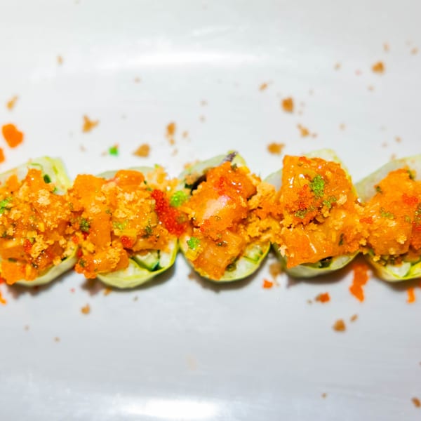 Five sushi rolls with orange topping and green garnish on a white plate at Hot Tuna Sushi Bar and Grille.