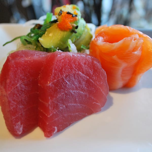 Fresh tuna and salmon sashimi with a side of seaweed salad and avocado on a white plate.