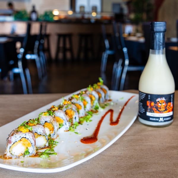 A plate of sushi rolls with orange sauce and greens, next to a bottle of sake.